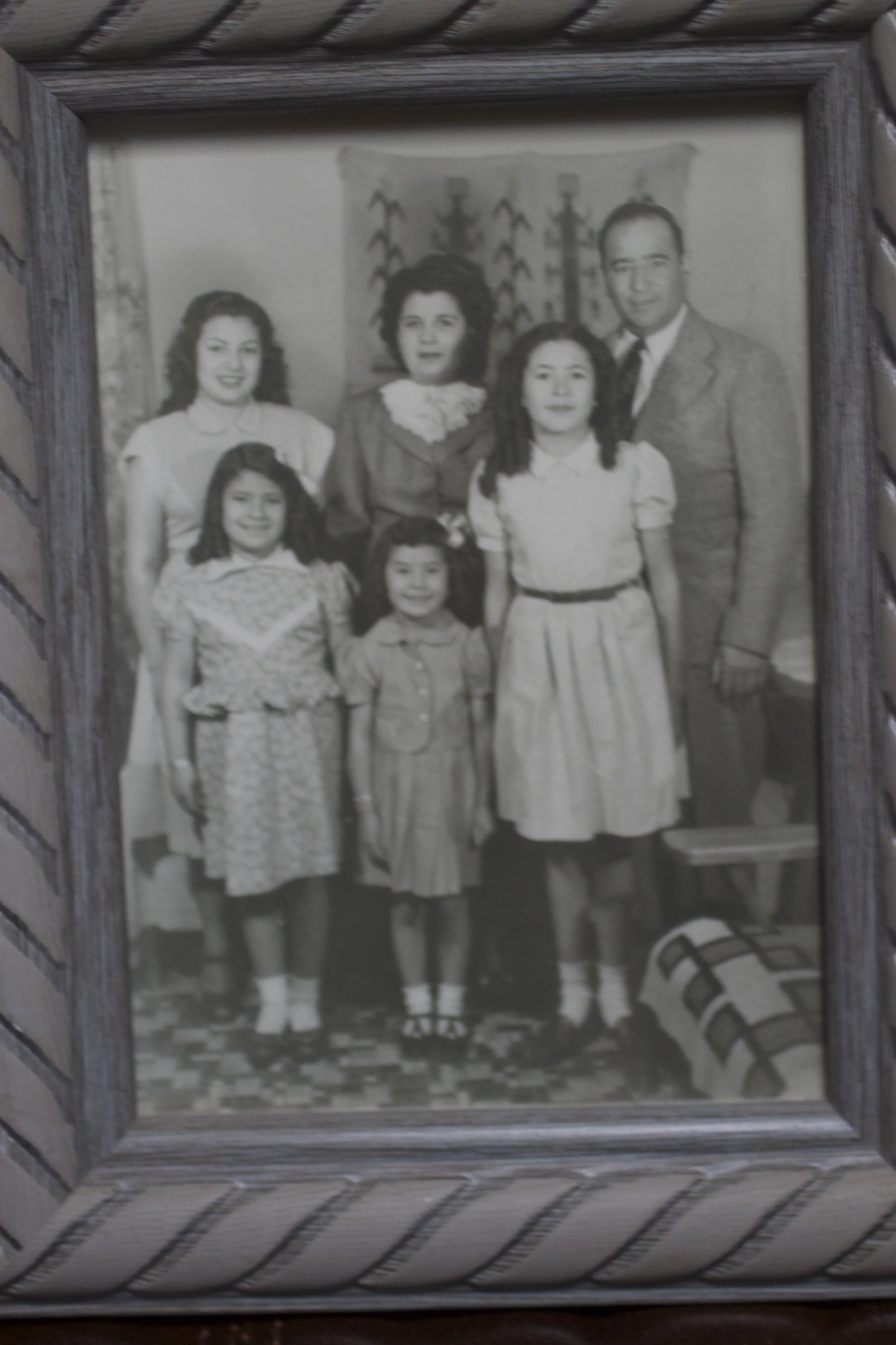 Black and white vintage family photo of five people, including two adult women, a man, and two young girls, posing in front of a curtain with a decorative pattern.