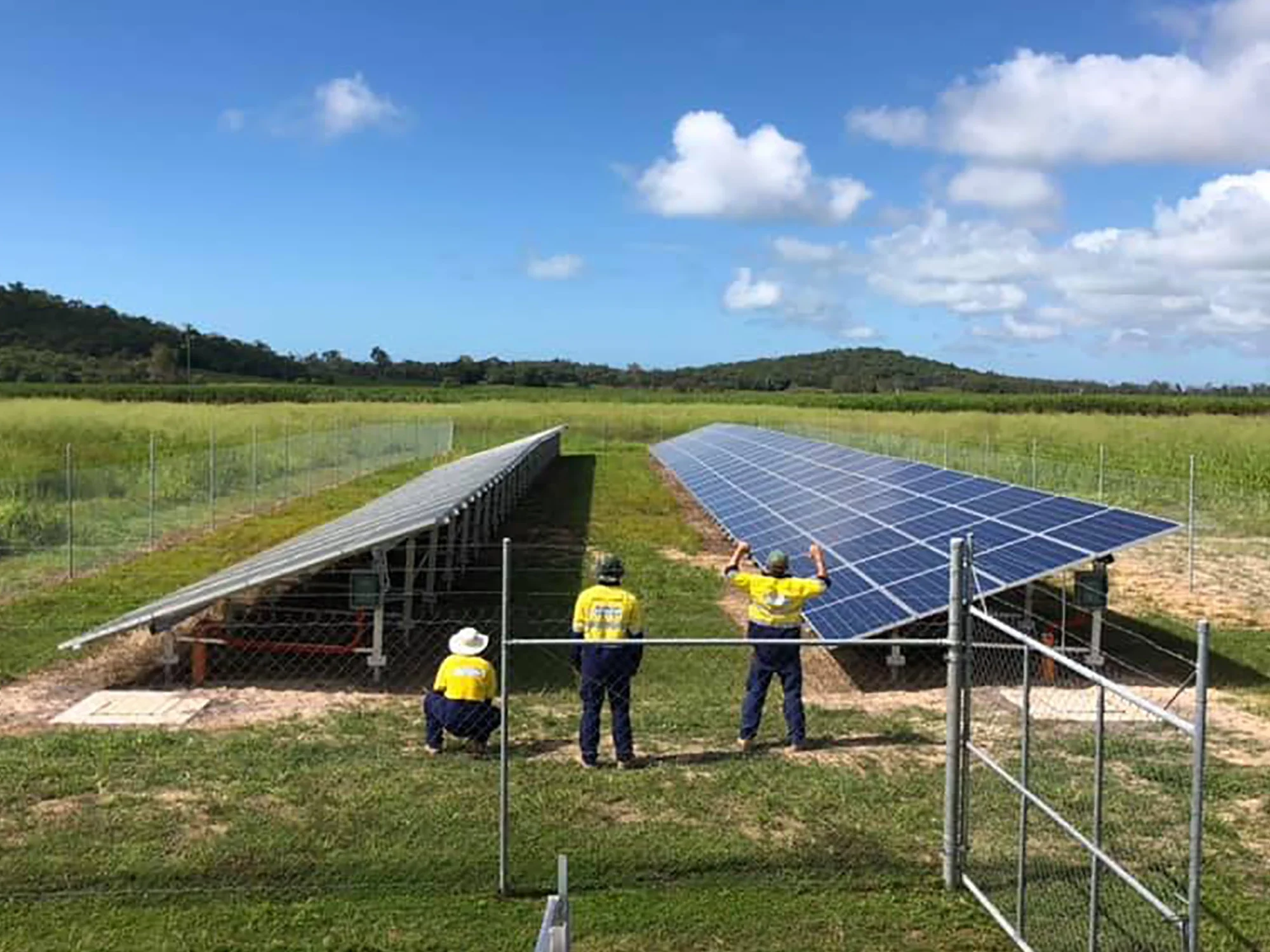 All Stacks Electrical Workers installing solar panels on a farm field with green hills and a partly cloudy blue sky in the background.