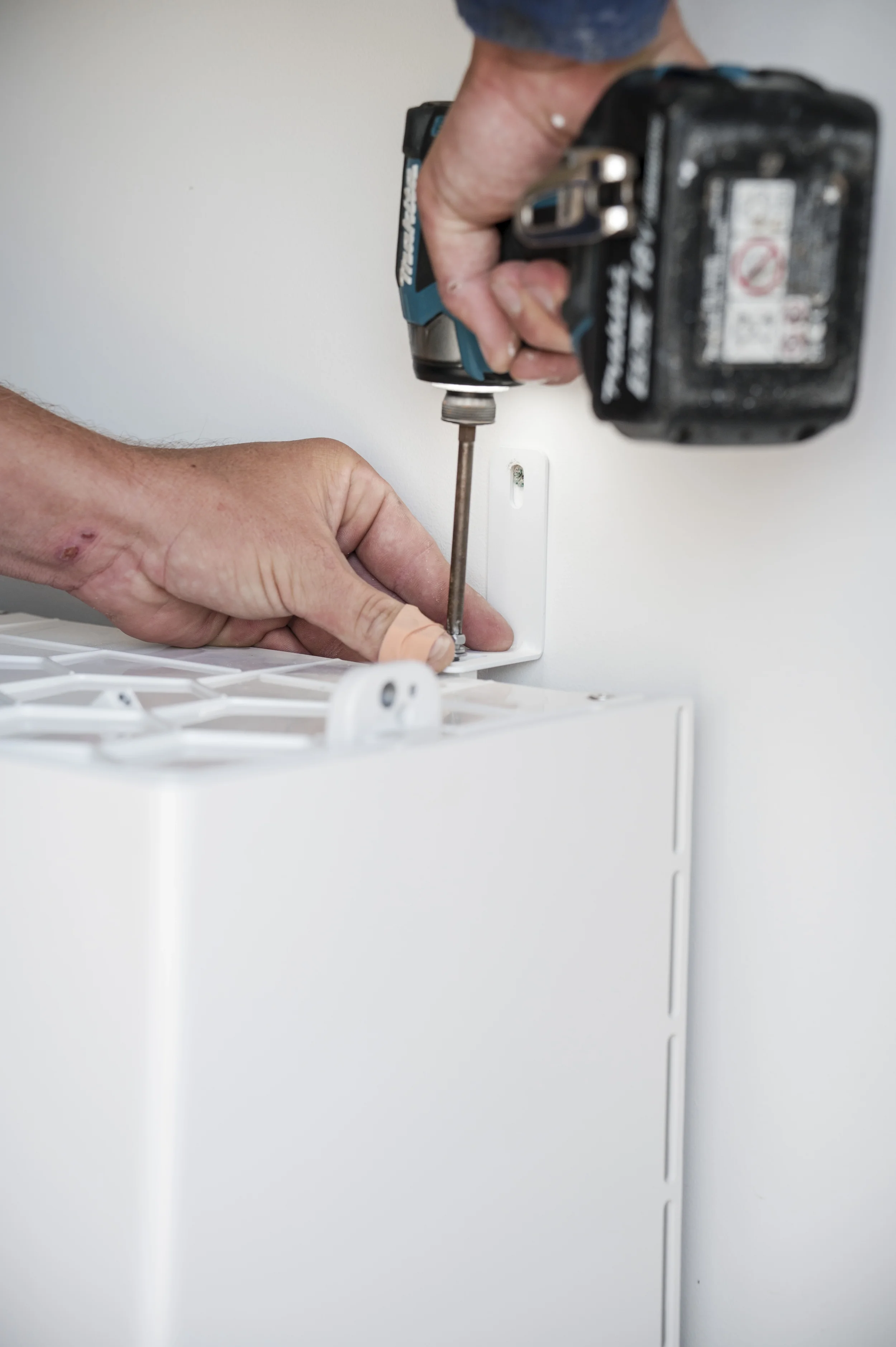 A person using a cordless drill to fasten a screw into a solar inverter