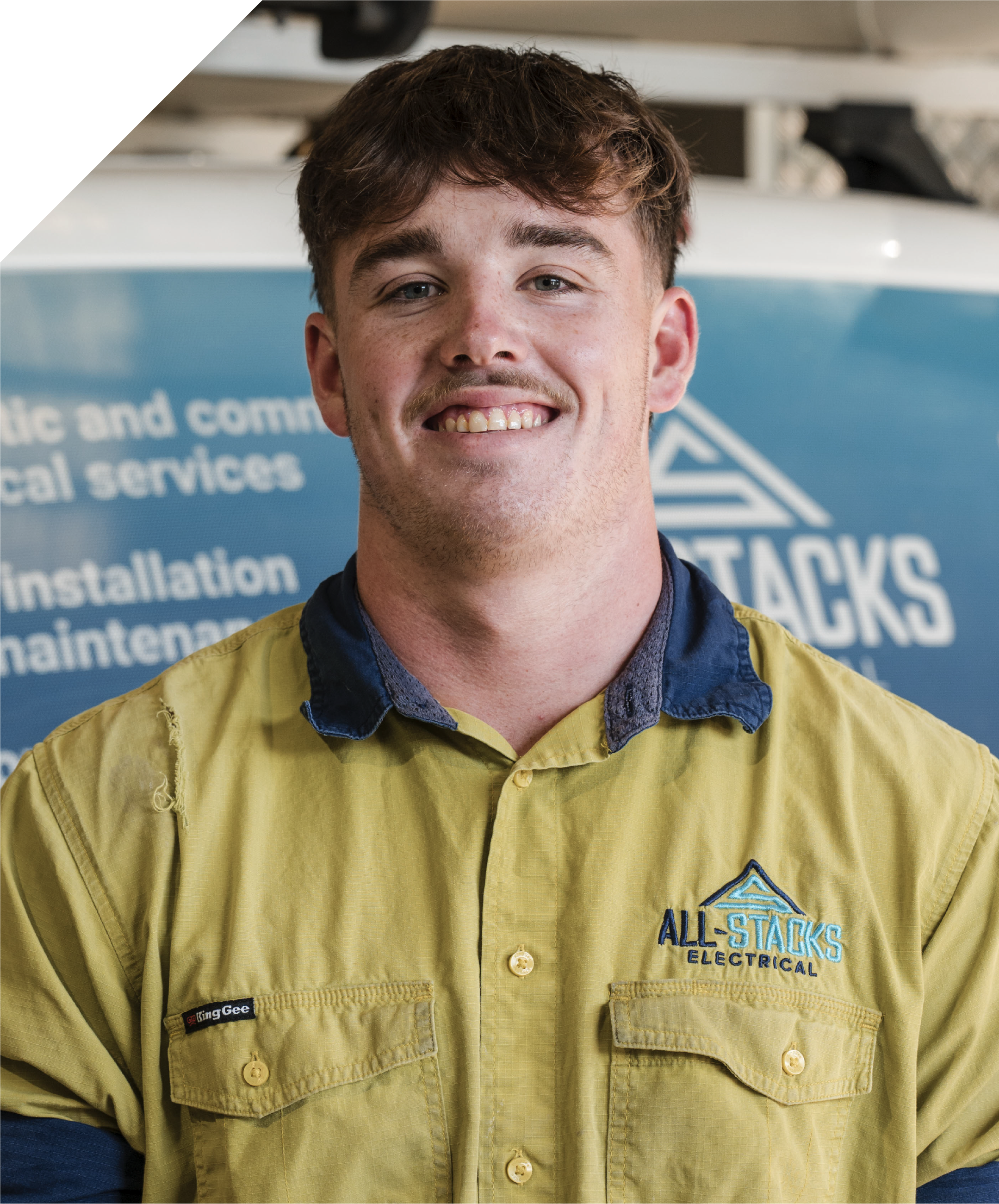 A smiling male worker wearing a yellow All Stacks Electrical work uniform, standing in front of All Stacks Electrical work van.