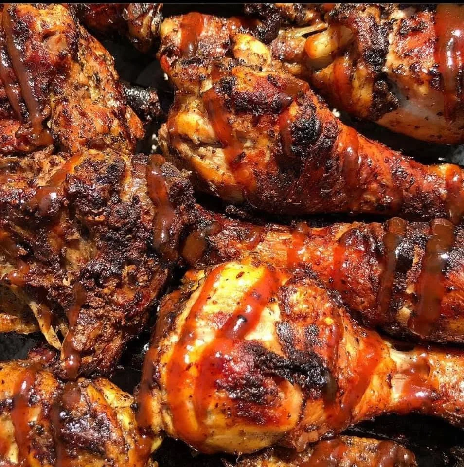 Close-up of grilled chicken drumsticks with a shiny glaze, charred spots, and drizzles of barbecue sauce.
