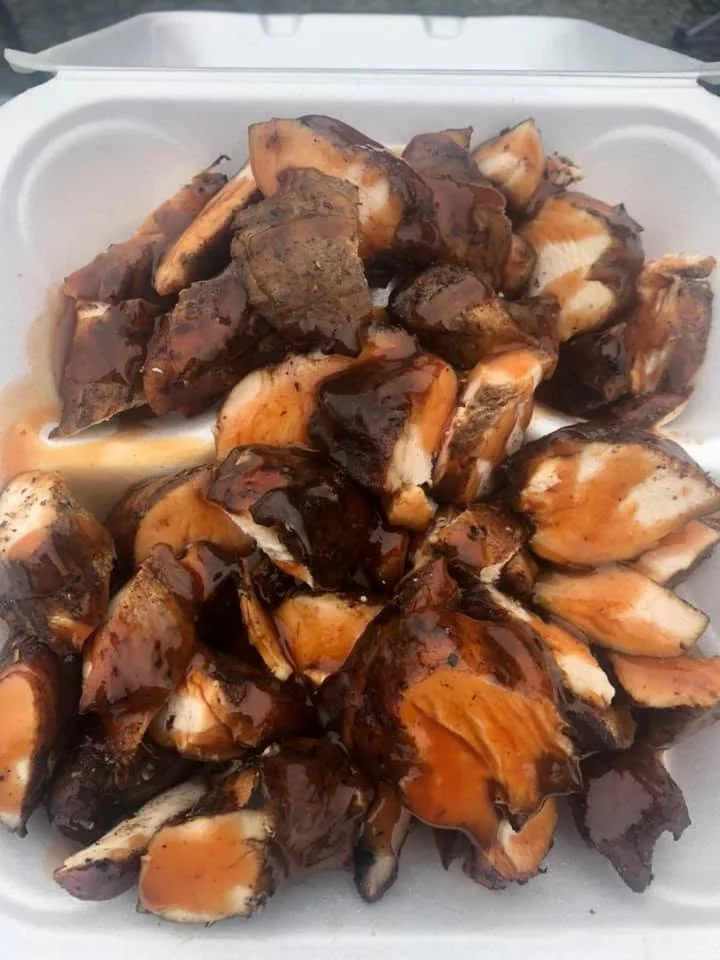Barbecue chicken pieces with dark barbecue sauce in a white styrofoam takeout container.