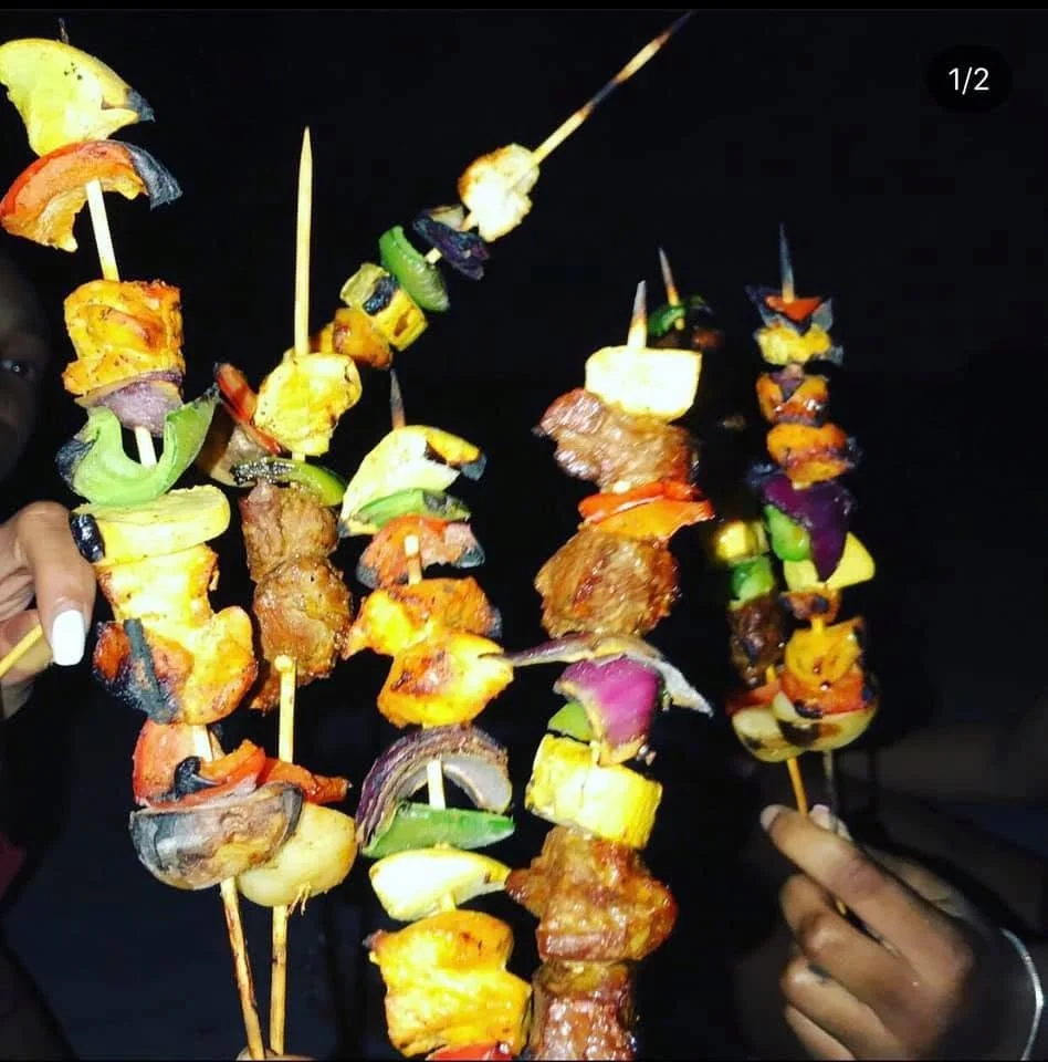 Skewers with grilled meat and colorful vegetables held by people in front of a dark background.