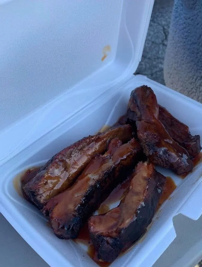 Barbecue pork ribs in a white takeout container with sauce.