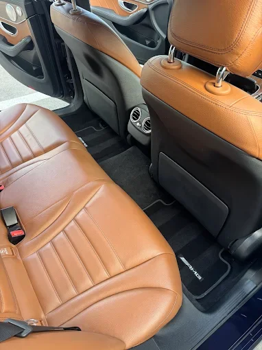 View of a car's interior showing tan leather seats, black floor mats, and rear air vents.