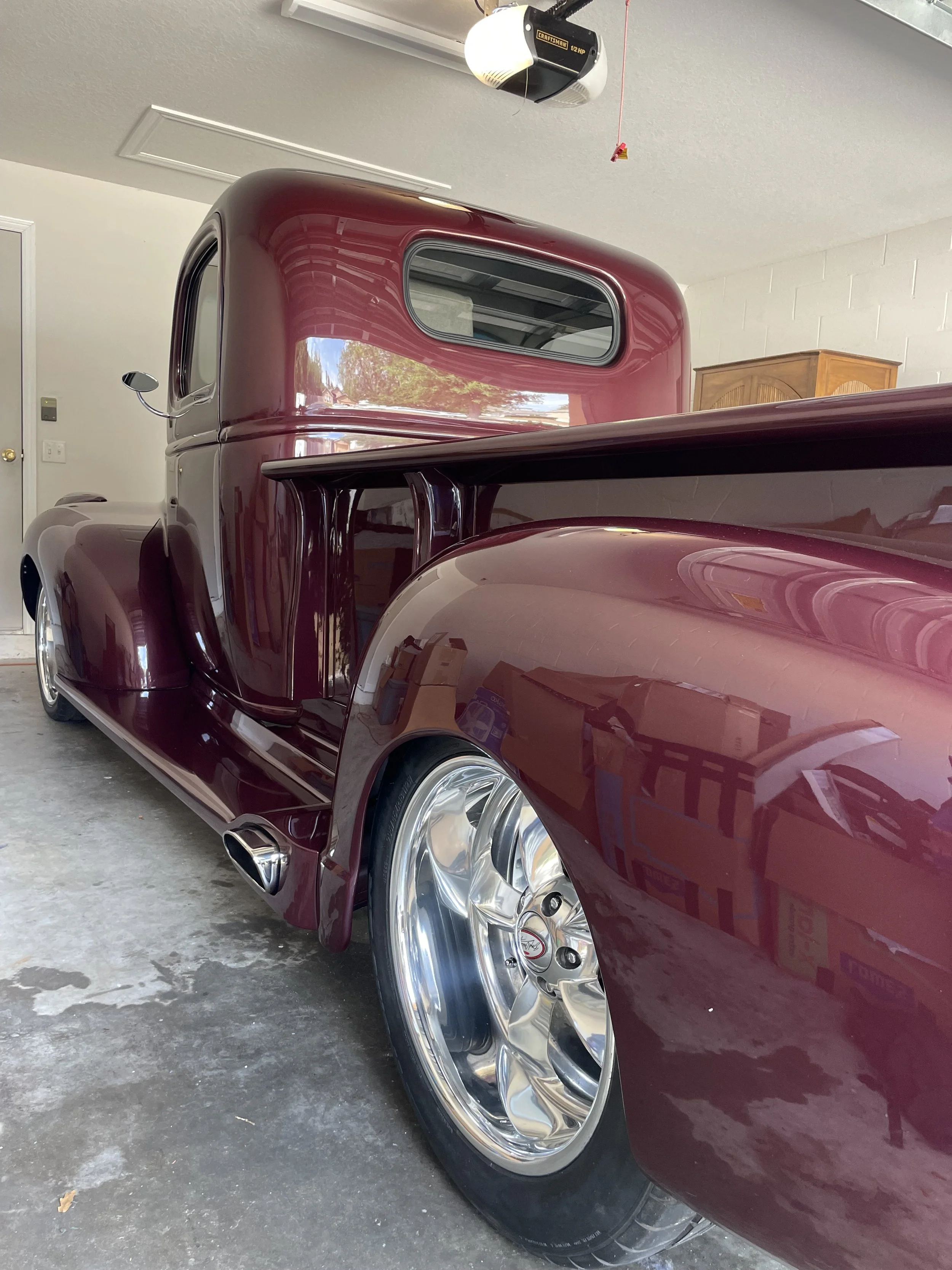 A vintage maroon pickup truck with chrome wheels parked in a garage.