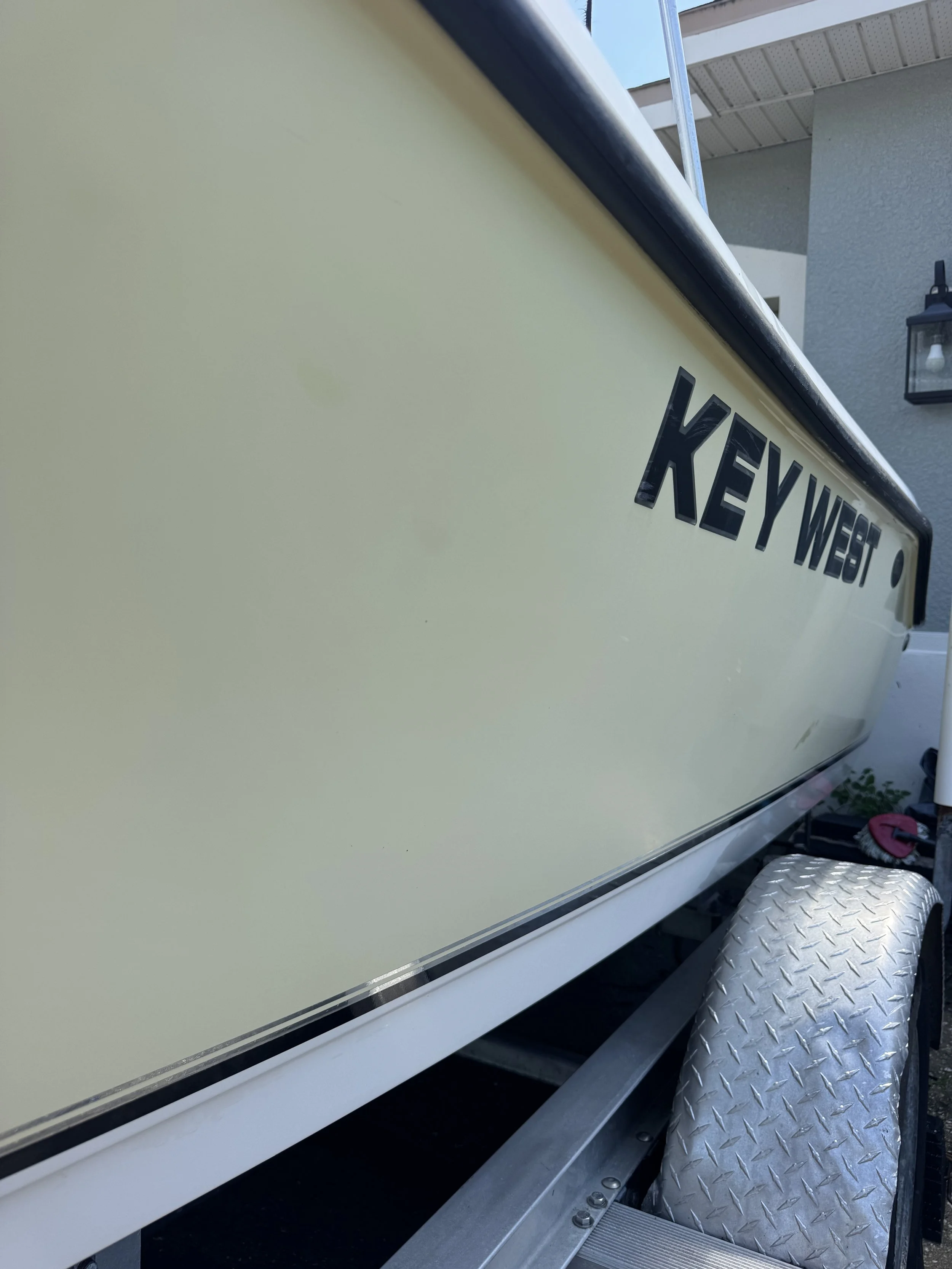 Close-up of a boat with yellow exterior paint, black lettering spelling 'KEY WEST,' aluminum diamond plate step, and metal trim.