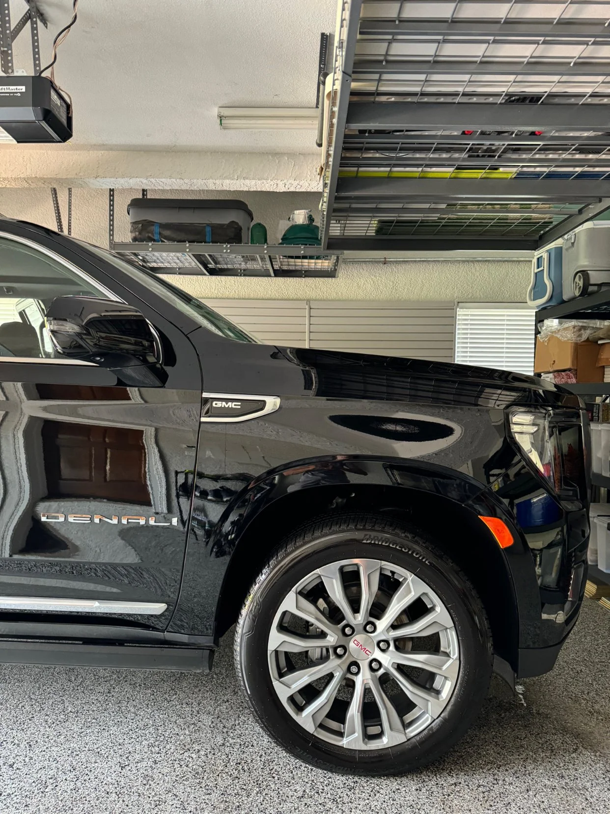 Black GMC Denali pickup truck parked in a garage with garage shelves and storage containers.