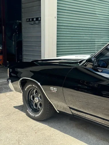 Close-up of a black vintage Chevrolet muscle car with SS badge on the front fender, parked outside a garage