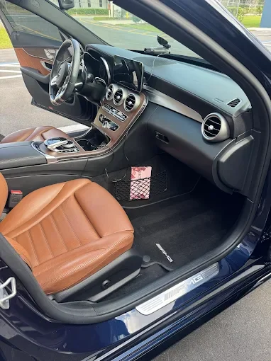 The interior of a luxury car showing the front passenger seat, dashboard, and steering wheel, with a brown leather seat and black interior accents.