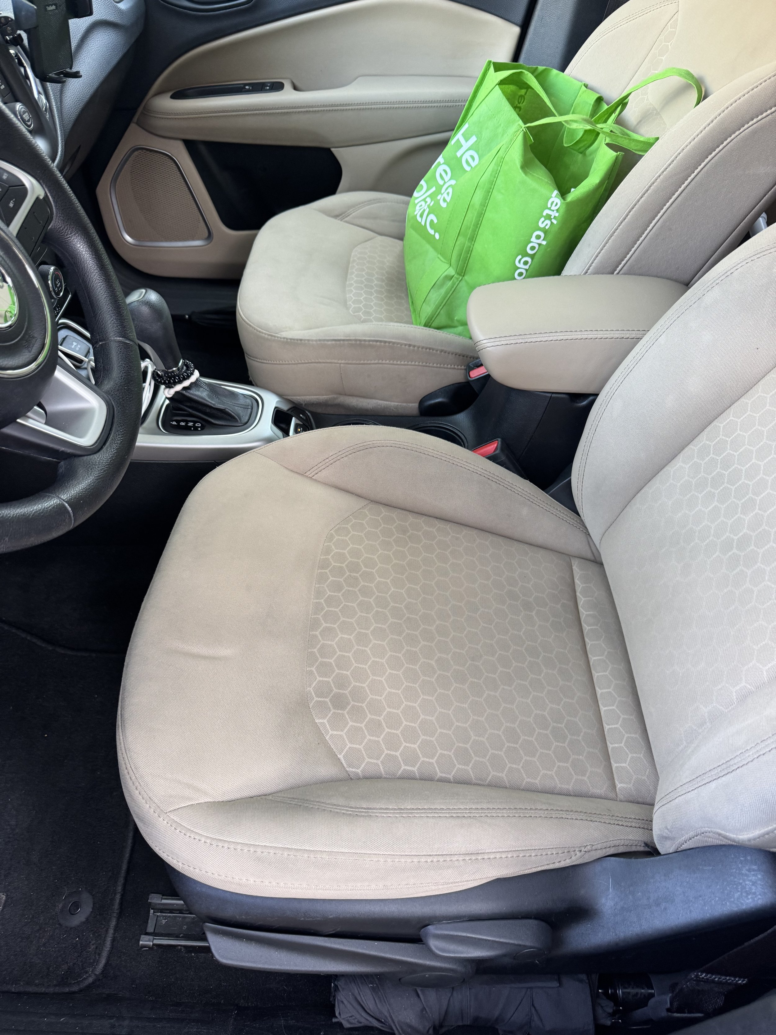 A beige car seat with a green reusable shopping bag on it inside a vehicle.