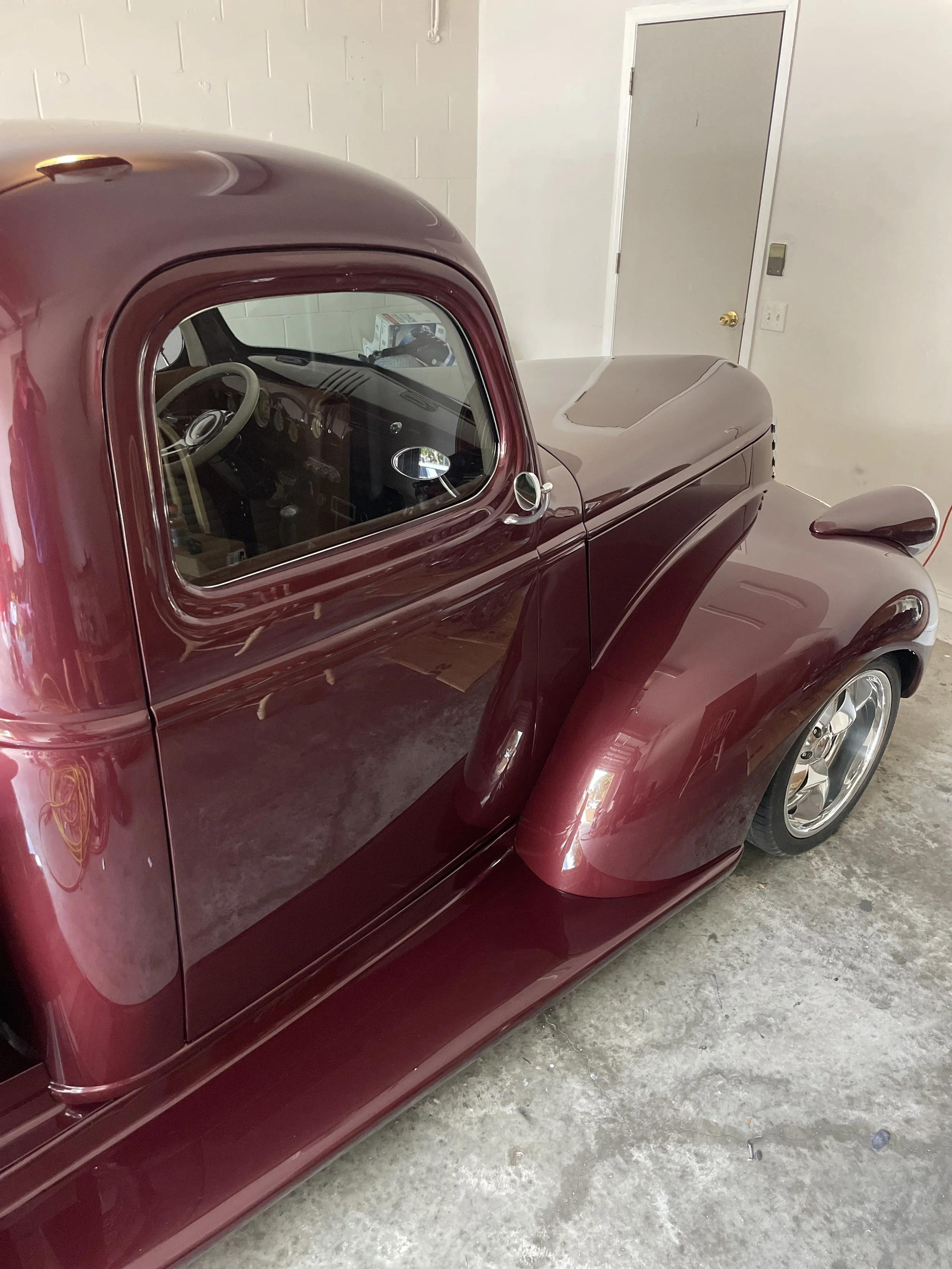 A vintage maroon car parked in a garage with concrete flooring and white walls.