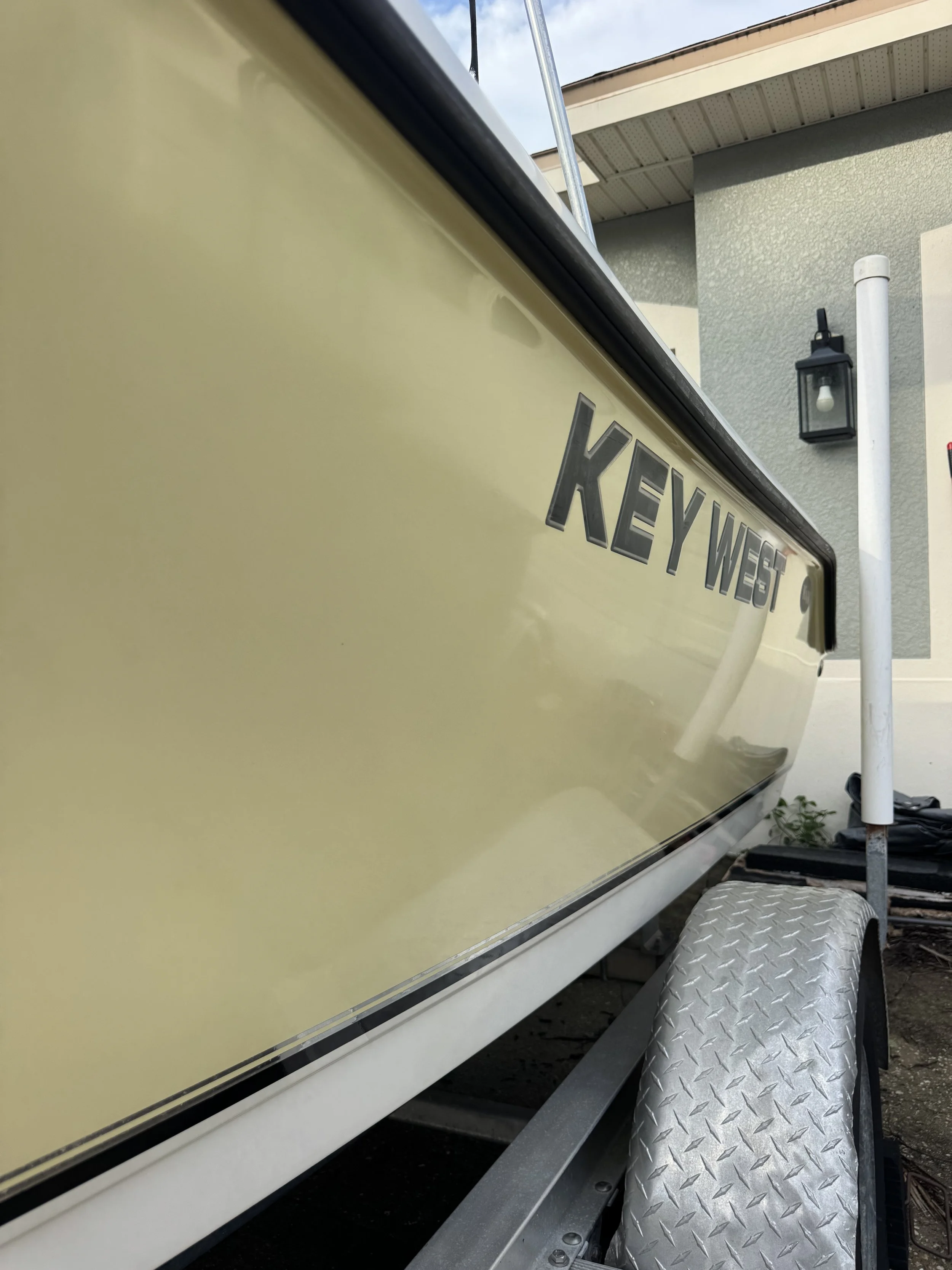 Close-up of a yellow food trailer with the name 'Key West' on it, parked outside a building with a gray textured wall and a lantern-style light fixture.