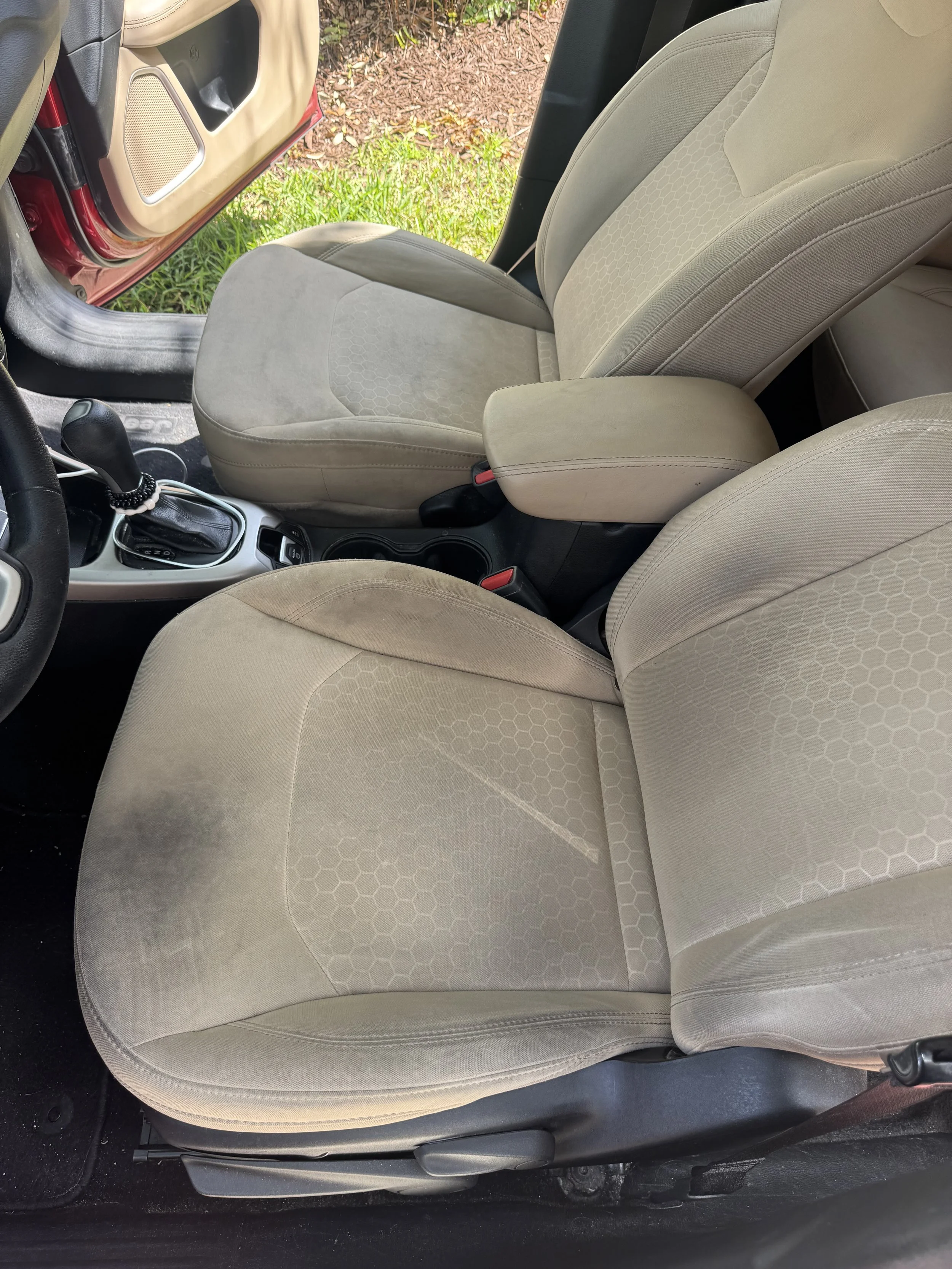 Front beige car seat with a honeycomb pattern on the seat and backrest, inside a vehicle with a black interior and a gearshift visible.