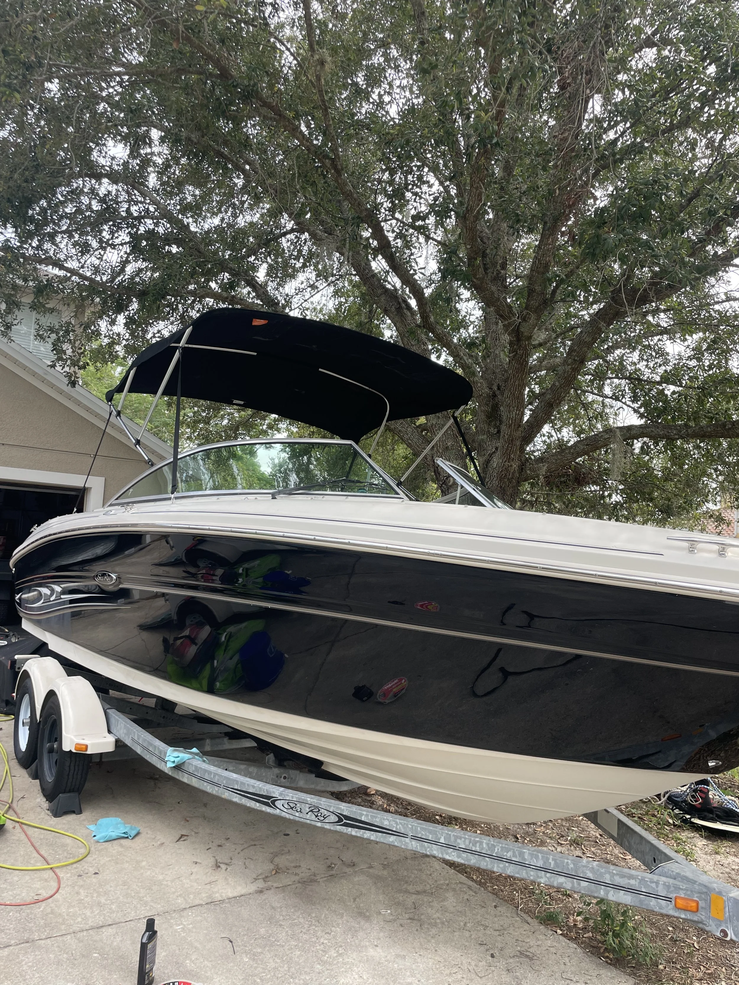 A black and white speedboat on a trailer parked on a driveway, with a large tree in the background.
