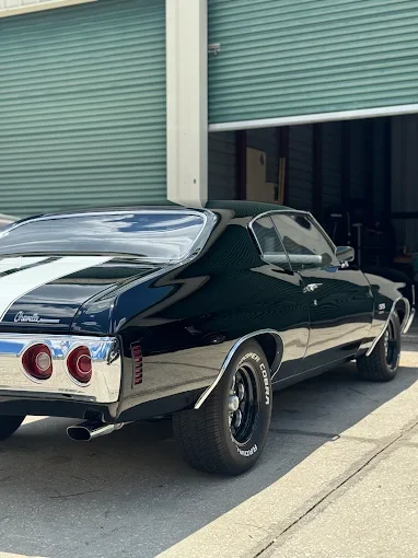 A black vintage Chevrolet car parked outside a garage with green doors.