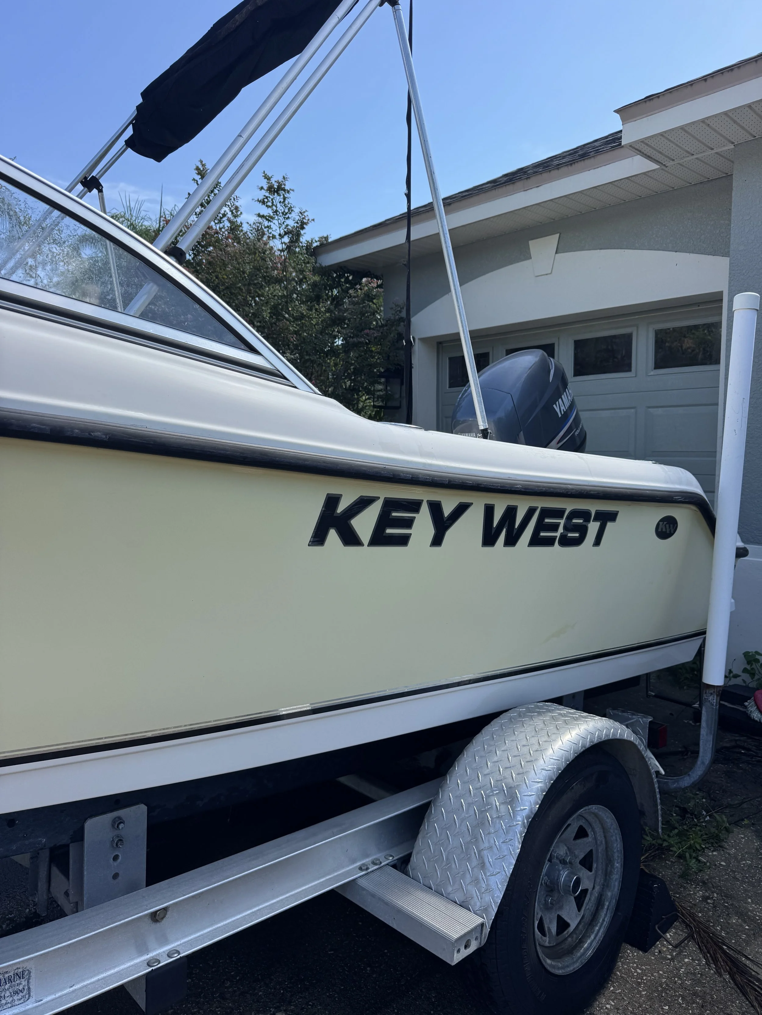 A boat with a Yamaha outboard motor on a trailer, parked in front of a house with trees in the background.