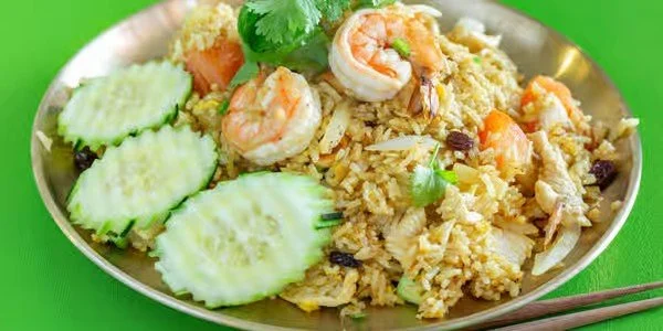 Plate of shrimp fried rice with cucumber slices on the side, garnished with cilantro, on a green table.
