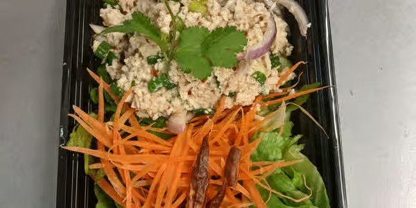 A black rectangular container with fresh vegetables like shredded carrots, lettuce, and a topping of quinoa salad garnished with cilantro.