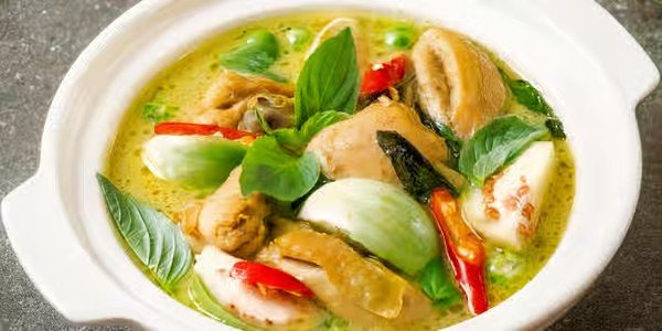 Bowl of Thai green curry with chicken, bamboo shoots, red chili, basil leaves, and coconut milk.