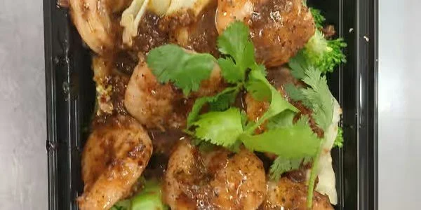 Close-up of cooked chicken drumsticks with herbs and seasoning in a black container.