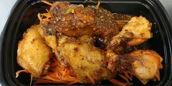 Cooked chicken pieces with sauce and shredded carrots in a black container.