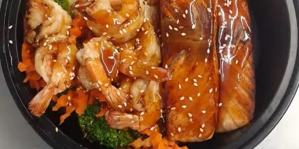 Shrimp with orange sauce and two spring rolls topped with sesame seeds, served with shredded carrots and broccoli in a black bowl.