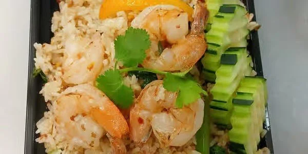 Shrimp and rice with slices of cucumber and cilantro garnished with a lemon wedge.