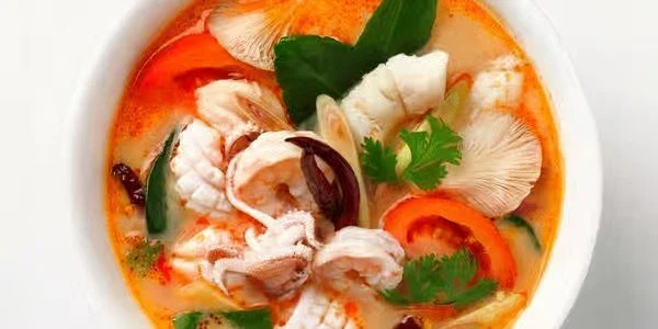A bowl of spicy seafood soup with pieces of fish, shrimp, vegetables, and herbs.