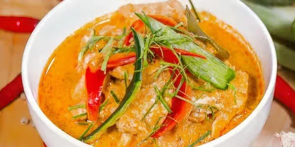 A bowl of Thai red curry with chicken, vegetables, and herbs.