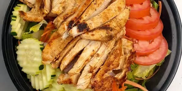 Grilled chicken slices topped with chopped tomatoes and surrounded by sliced cucumbers and shredded carrots on a black plate.