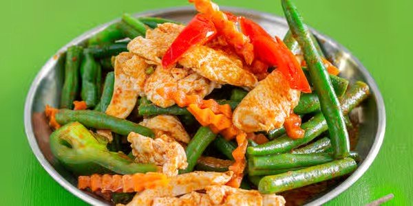 Stir-fried fish with green beans and sliced carrots in a silver bowl on a green surface.