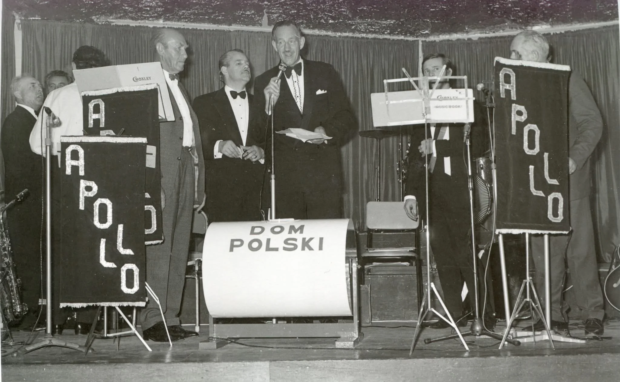 Archival photo of a formal concert on the Dom Polski stage, with POLSKA banners.