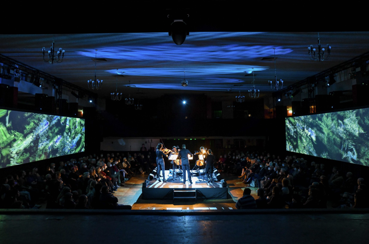 Orchestra performing on stage at Dom Polski Adelaide, with the audience seated around the hall.