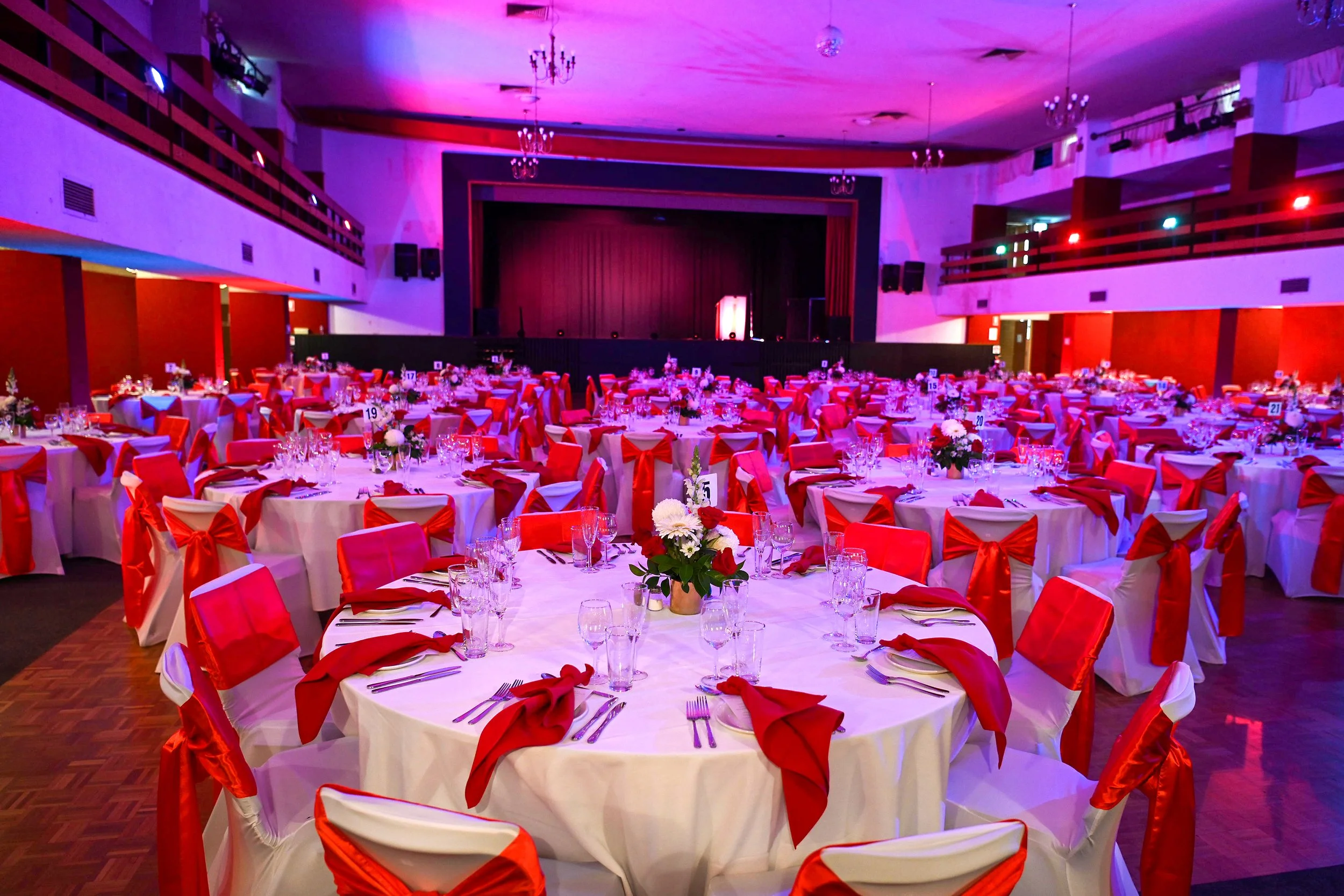 Balcony Hall set for a banquet with round tables, red chair sashes and floral centrepieces.