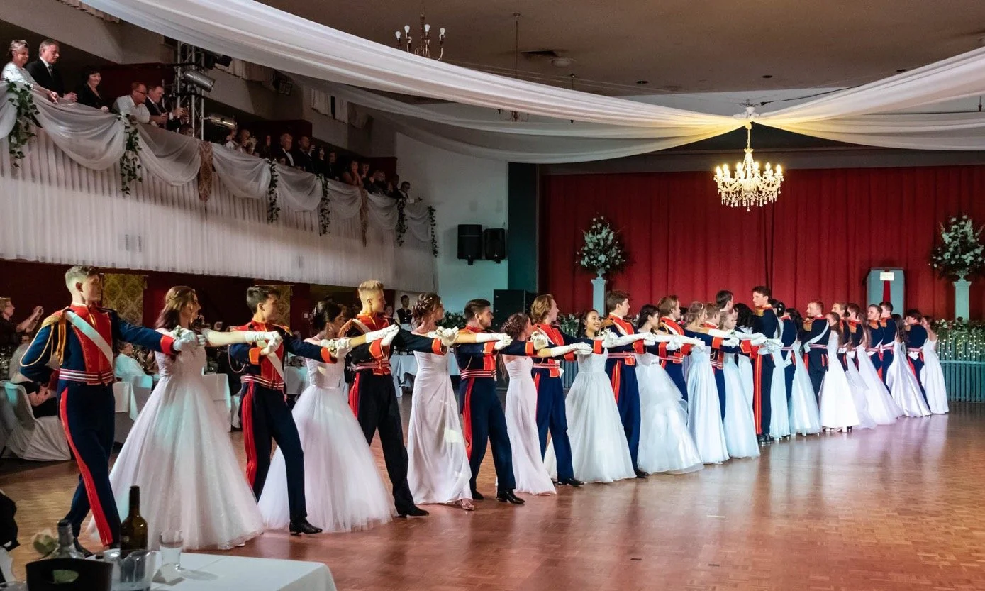 Folk dancers in blue, red and white costumes performing in the Balcony Hall.