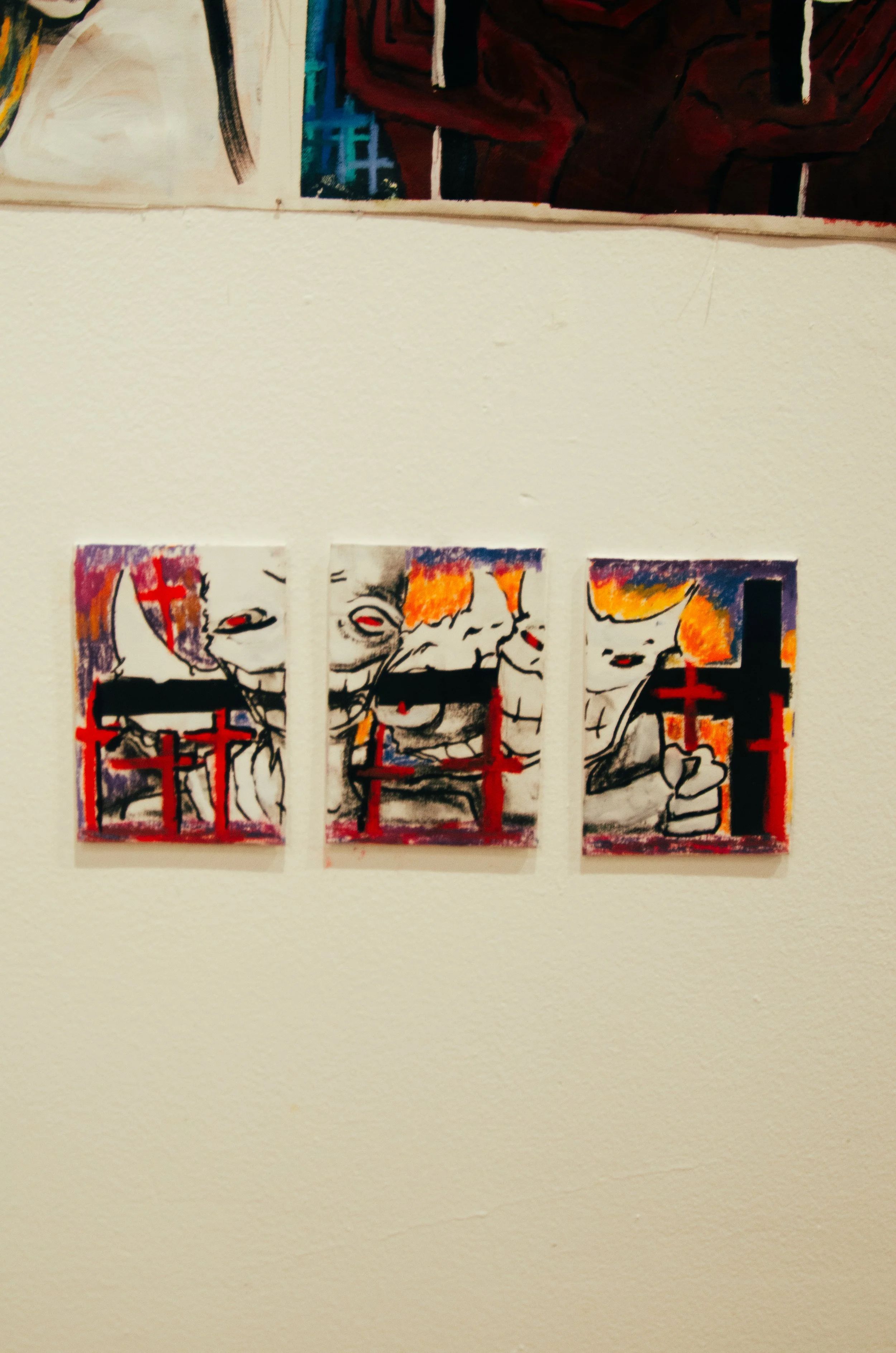 Three small posters or prints on a wall featuring black-and-white illustrations of smiling children with colorful backgrounds and red cross symbols.