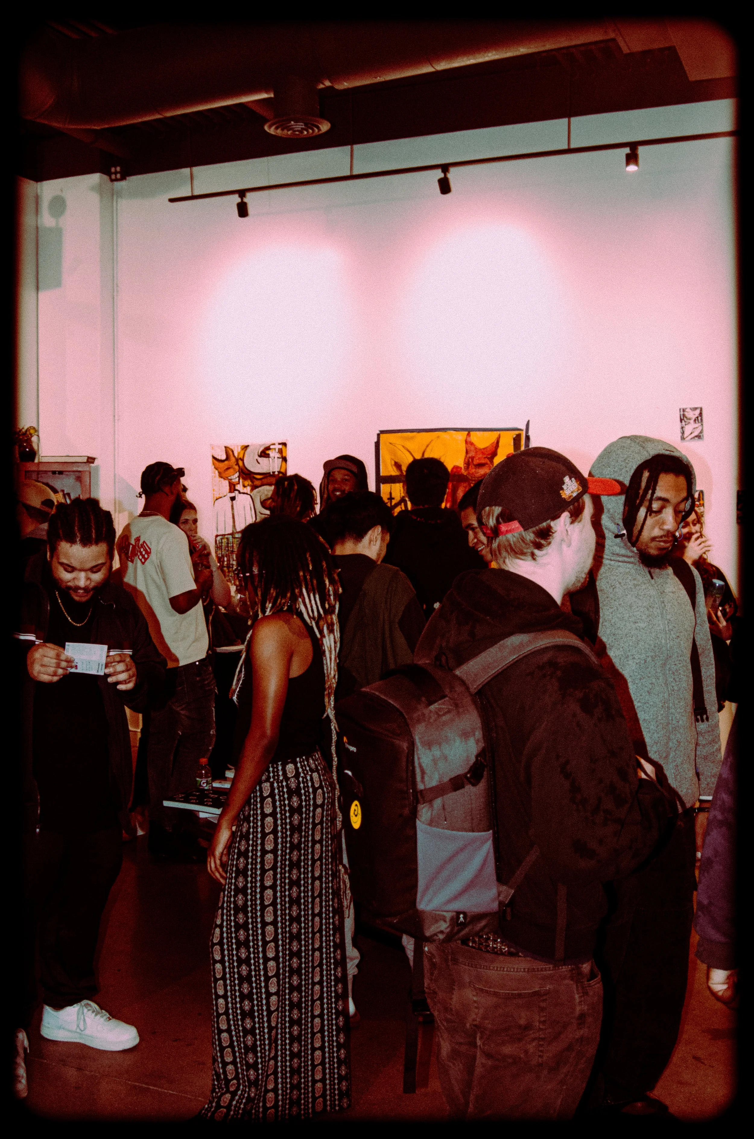 A group of people gathered in an art gallery with paintings on the wall, some browsing and others engaged in conversation.
