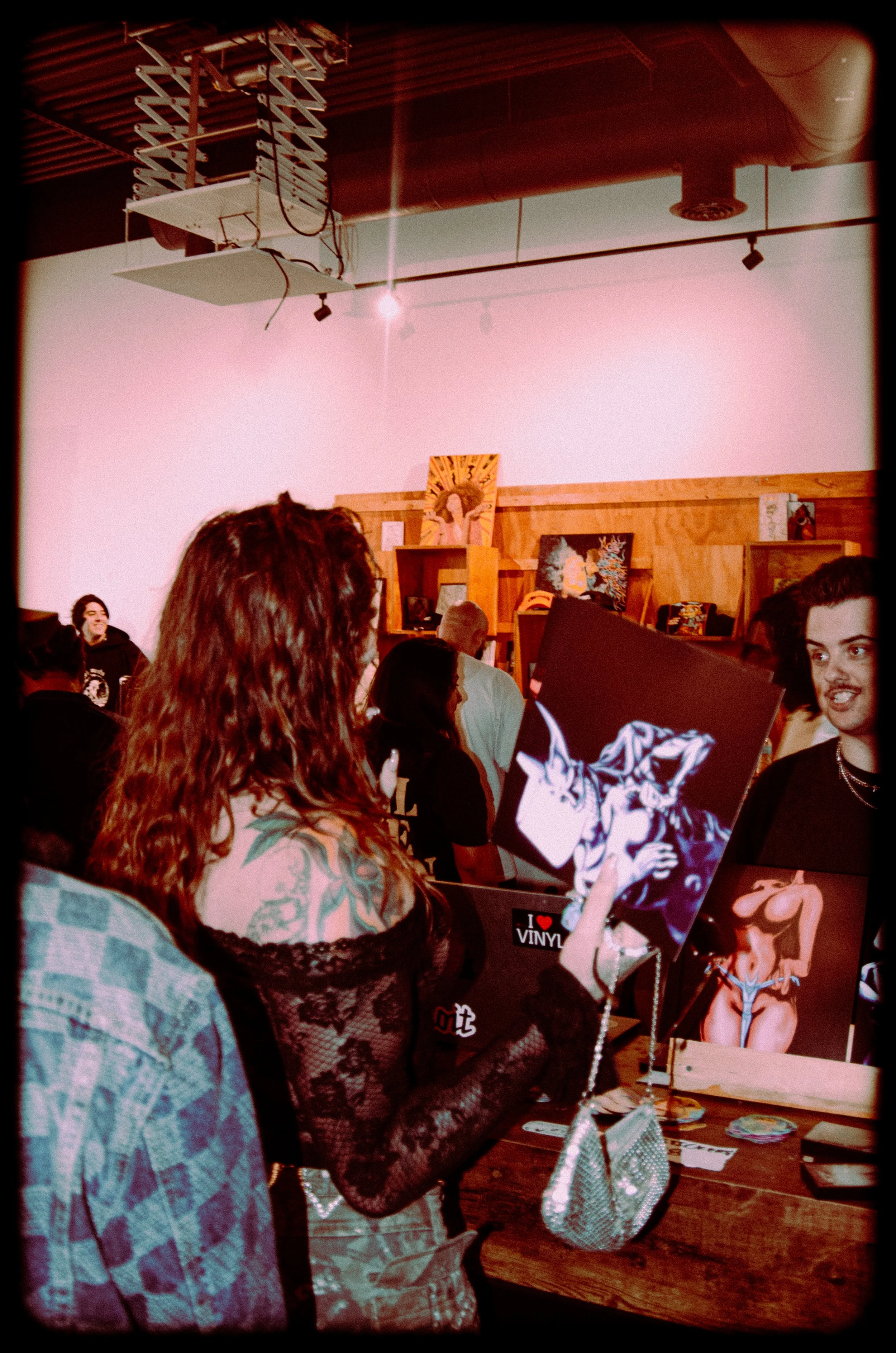 People at an art or pop culture event, closely examining and discussing various vinyl album covers displayed on a table.