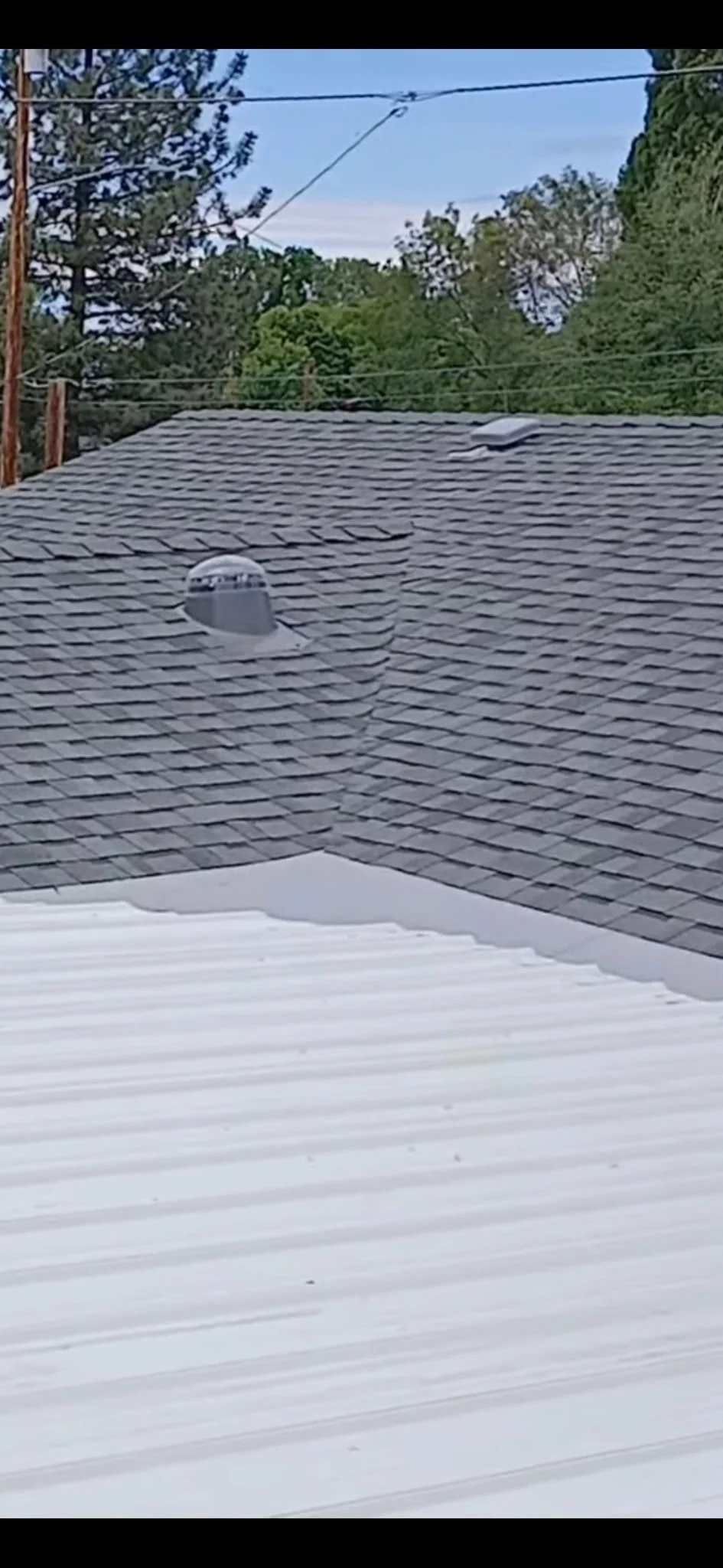 View of a roof with shingles, two attic vents, and a snowy foreground with snow-covered surface.