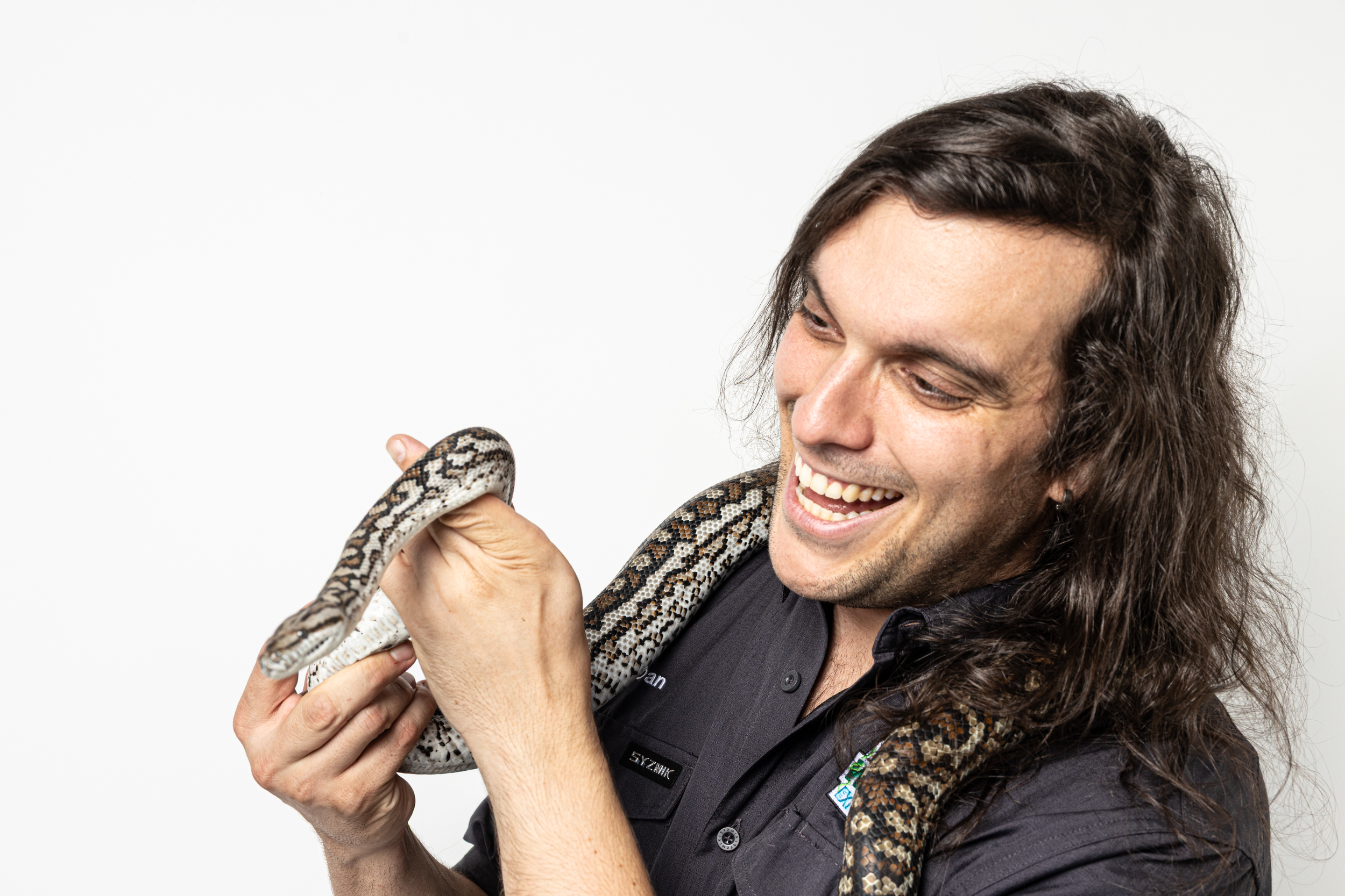 Man with long dark hair smiling while holding a carpert python.