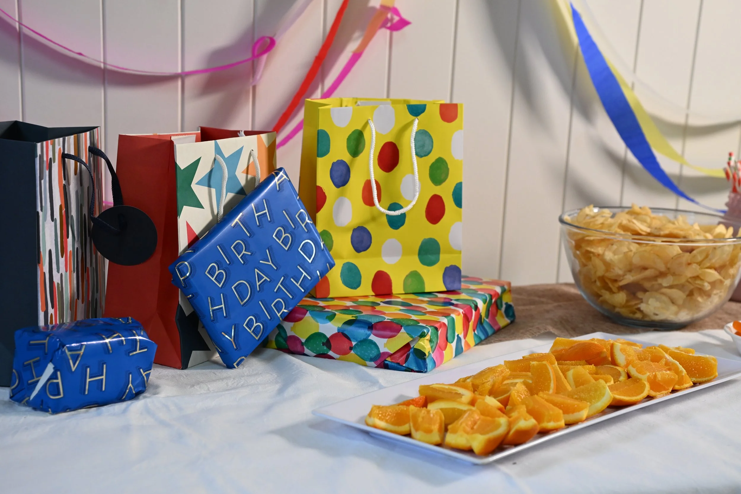 Colorful birthday party table with gift bags, food, and decorations.