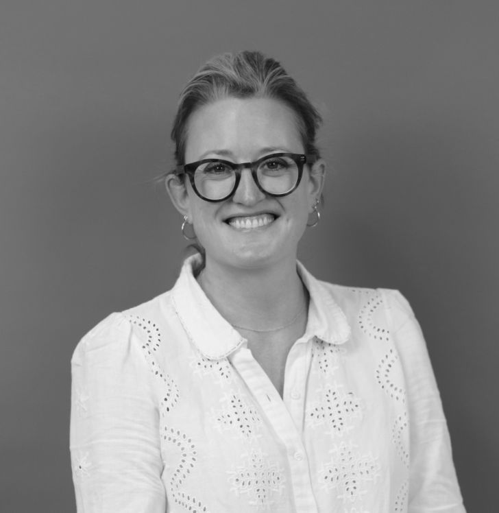 A woman with short hair, glasses, and hoop earrings smiling at the camera against a plain background.