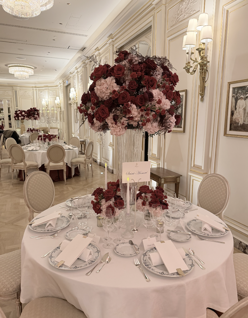 Table de banquet élégante décorée de fleurs rouges et roses, dans une salle de réception somptueuse avec murs ornés, chandeliers et portraits