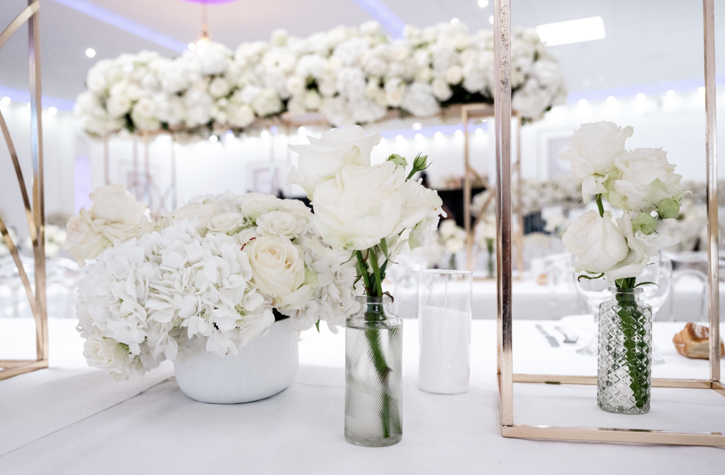 Vases avec des fleurs blanches, notamment des roses et des hortensias, décorant une table lors d'une réception ou d'un événement 