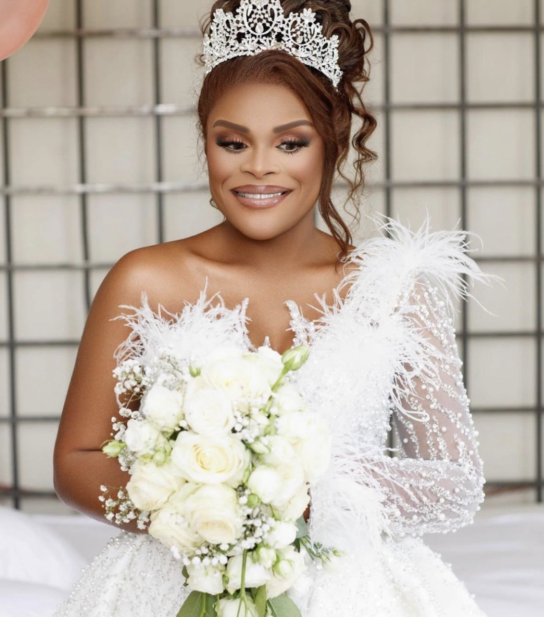 Une mariée souriante en robe de mariage blanche, portant une couronne en dentelle et tenant un bouquet de fleurs blanches.