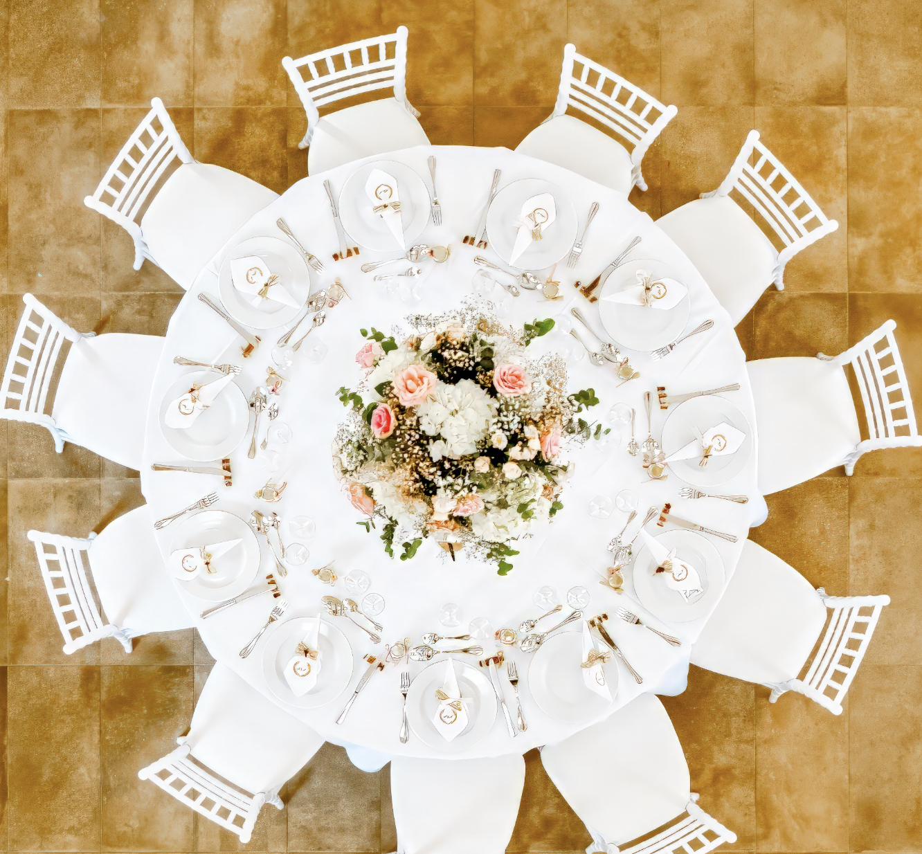Table ronde décorée d'un centre de fleurs avec des assiettes, des verres, des couverts et des serviettes, entourée de huit chaises blanches