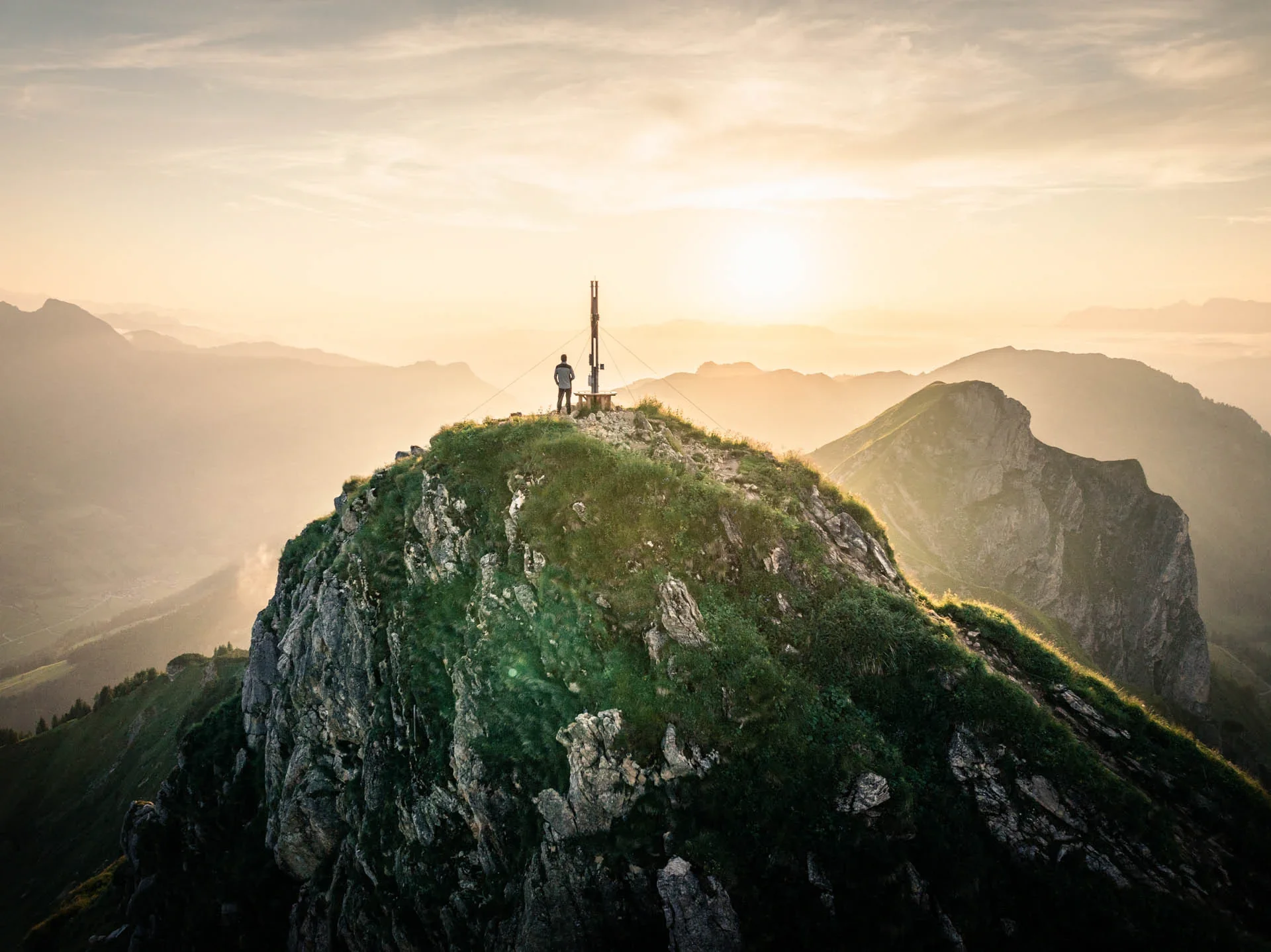 Ein Wanderer steht am Gipfelkreuz in den österreichischen Bergen bei Sonnenaufgang – der Moment, in dem Dominik Lüdtke seine Liebe zur Landschaftsfotografie entdeckte.