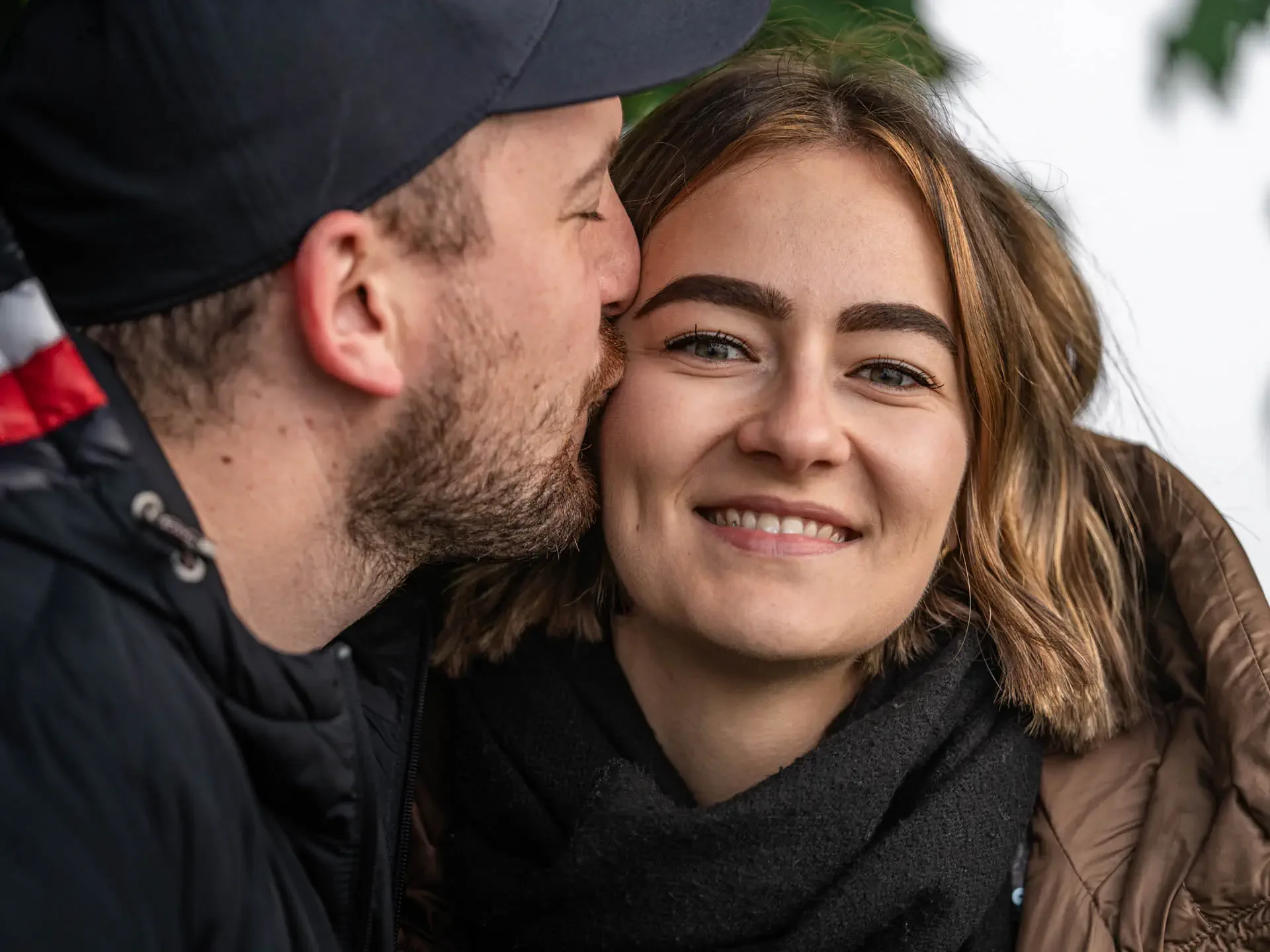 Ein Mann küsst eine lachende Frau im Freien. Aufgenommen bei einem Paarshooting mit Dominik Lüdtke