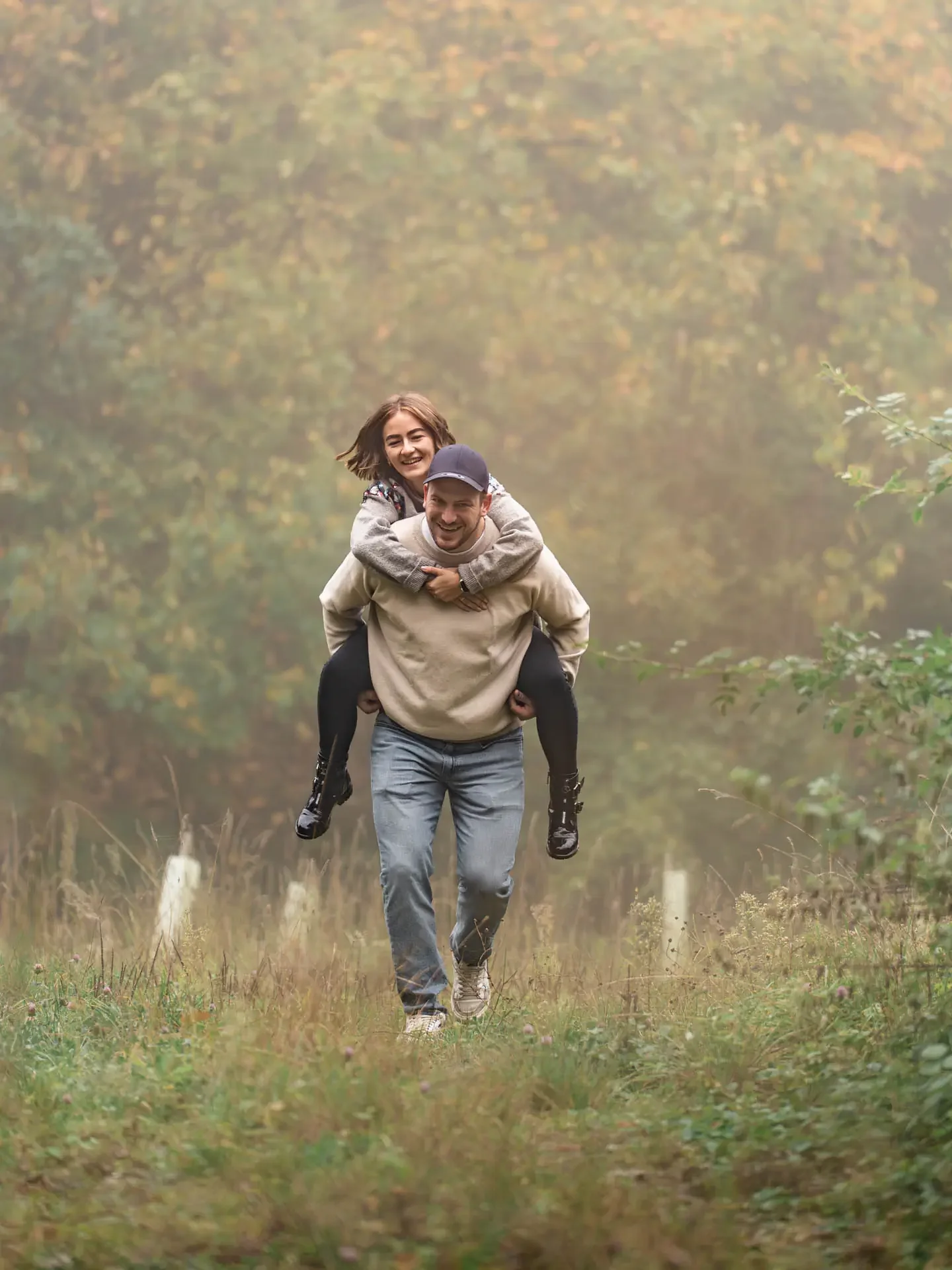 Glückliches Paar beim Huckepack-Spaziergang im Nebel – lebendige Lovestory-Fotografie.